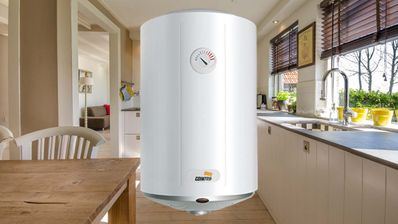 Termo eléctrico de color blanco instalado en la pared de un baño, con las tuberías de entrada y salida de agua visibles en la parte inferior.