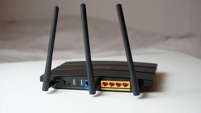 Parte trasera de un router inalámbrico negro con tres antenas externas, puertos Ethernet amarillos y conexiones USB.