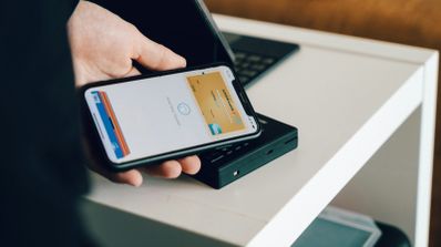 Ilustración conceptual de un smartphone con símbolo NFC, tarjetas de crédito y un escudo de seguridad, representando los riesgos de fraude en pagos móviles como Apple Pay y Google Wallet.