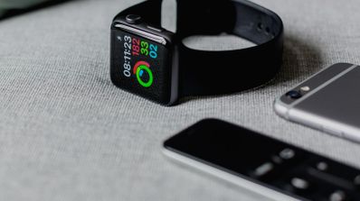 Primer plano de un Apple Watch Series 9 con sensores de salud activos junto a dos iPhone, ilustrando la recolección de datos biométricos en wearables.