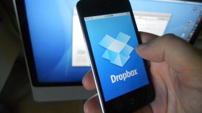 Una persona tiene un móvil con Dropbox en la pantalla y detrás un ordenador