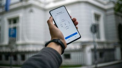 Primer plano de un smartphone mostrando una alerta de 'Llamada Sospechosa' de una aplicación de seguridad, con un edificio gubernamental desenfocado al fondo.