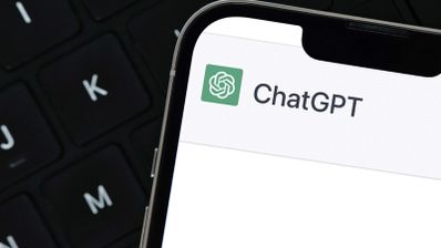 Primer plano de un teléfono móvil mostrando el logotipo y nombre de ChatGPT sobre un teclado de ordenador portátil.