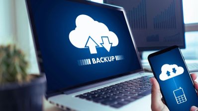 Ordenador portátil y teléfono móvil mostrando iconos de sincronización de copias de seguridad en la nube con la palabra backup.