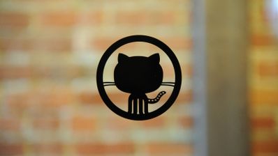 Logotipo negro de GitHub (Octocat) centrado sobre un fondo de pared de ladrillos desenfocado.