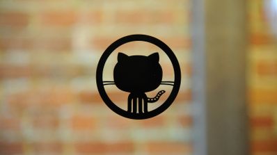 Logotipo negro de GitHub (Octocat) centrado sobre un fondo de pared de ladrillos desenfocado.
