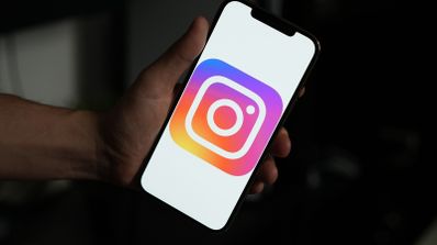 Mano sujetando un teléfono móvil que muestra el logotipo de Instagram a pantalla completa en una habitación oscura.