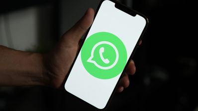 Mano sujetando un teléfono móvil que muestra el logotipo de WhatsApp sobre un fondo blanco en pantalla.