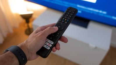 Persona sosteniendo un mando a distancia negro frente a un televisor inteligente con pantalla azul.
