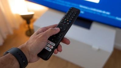 Primer plano de una mano sosteniendo un mando a distancia frente a una televisión inteligente con pantalla azul.