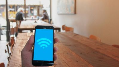Mano sosteniendo un teléfono móvil con el icono de conexión Wi-Fi en pantalla en el interior de una cafetería.