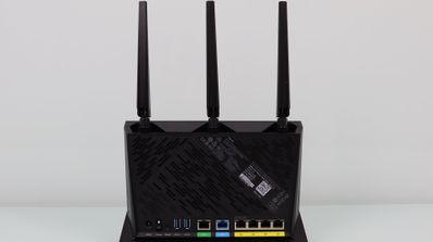 Panel posterior de un router ASUS RT-AX86U que muestra tres antenas externas, puertos Ethernet amarillos, un puerto WAN azul y conexiones USB.
