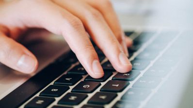 Primer plano de una persona escribiendo en el teclado de un ordenador portátil con teclas negras.