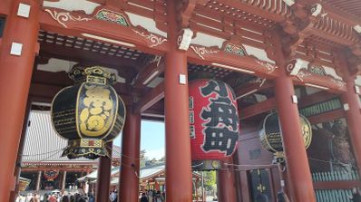 Grandes faroles rojos y negros colgados de la estructura de madera roja de una puerta de entrada tradicional japonesa.