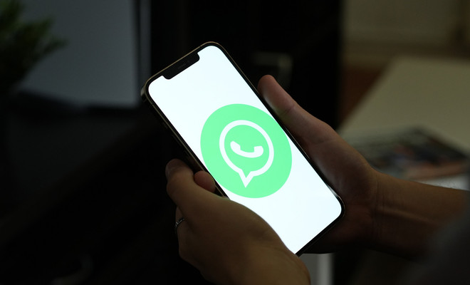 Primer plano de unas manos sujetando un smartphone que muestra el logotipo de la aplicación WhatsApp en una pantalla blanca brillante.