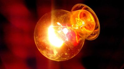 Bombilla de filamento incandescente encendida emitiendo una luz cálida y anaranjada sobre un fondo oscuro.