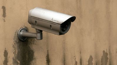Cámara de videovigilancia de tipo bala instalada en una pared exterior con manchas de humedad.