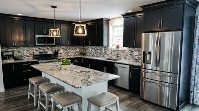 Cocina moderna con armarios negros, encimera de mármol blanco y frigorífico de acero inoxidable de doble puerta.