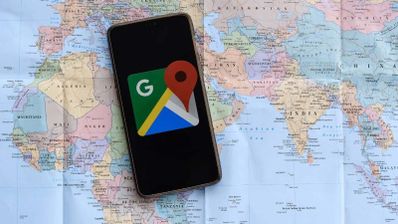 Teléfono inteligente con el logotipo de Google Maps en pantalla descansando sobre un mapa físico del mundo que muestra África, Europa y Asia.
