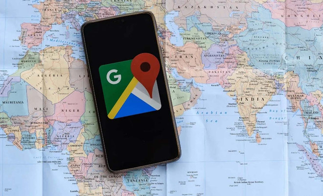 Teléfono inteligente con el logotipo de Google Maps en pantalla descansando sobre un mapa físico del mundo que muestra África, Europa y Asia.