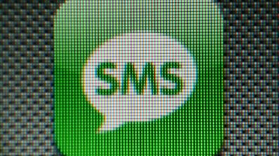 Primer plano de una pantalla digital mostrando el icono verde de una aplicación de mensajes con el texto SMS en una burbuja de chat blanca.
