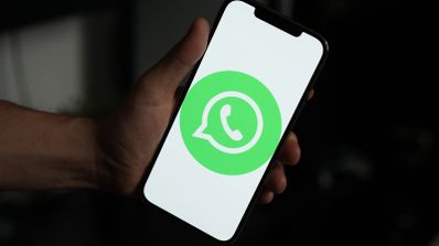 Mano sosteniendo un teléfono móvil inteligente que muestra el logotipo de WhatsApp sobre un fondo blanco en la pantalla.