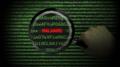 Una mano sostiene una lupa sobre líneas de código informático verde, resaltando la palabra MALWARE en letras rojas.