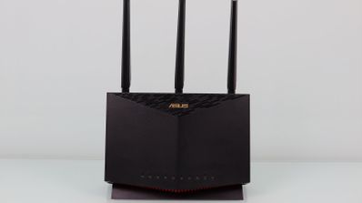 Router ASUS RT-AX86U de color negro con tres antenas externas verticales y luces LED indicadoras de estado en la base sobre un fondo blanco.