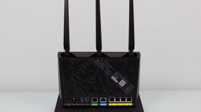 Parte trasera de un router inalámbrico negro con tres antenas externas verticales y múltiples puertos de conexión Ethernet y USB.