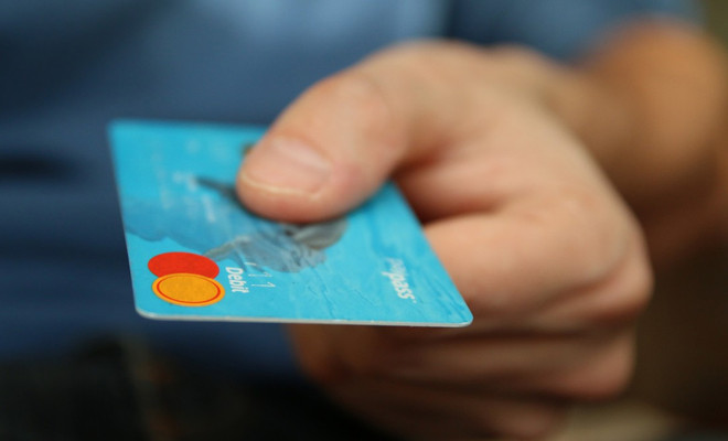 Primer plano de una mano sosteniendo una tarjeta bancaria de color azul con logotipos de pago sobre un fondo desenfocado.