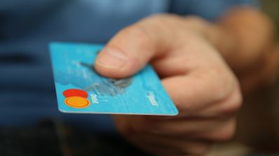 Primer plano de una mano sosteniendo una tarjeta bancaria de color azul con logotipos de pago sobre un fondo desenfocado.