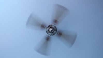 Primer plano de las aspas de un ventilador de techo girando a gran velocidad sobre un fondo claro.