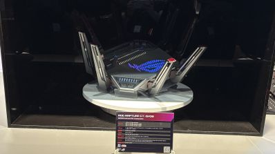 Router gaming ASUS GT-BN98 con ocho antenas externas y logotipo iluminado expuesto en una vitrina.