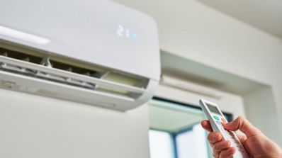 Mano utilizando un mando a distancia para configurar un equipo de aire acondicionado split en una vivienda.