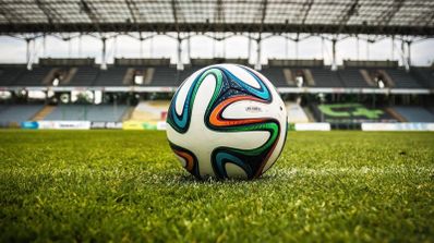 Primer plano de un balón de fútbol sobre el césped de un estadio vacío bajo la estructura de la grada.