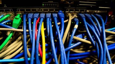 Conexiones de cables Ethernet de color azul, verde y amarillo conectados a los puertos de un switch de red en un rack.