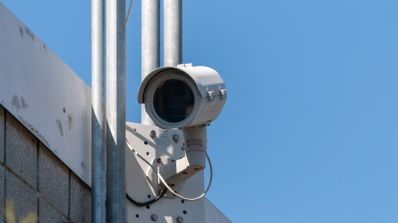 Cámara de vigilancia tipo bala instalada en un poste metálico en el exterior de un edificio.