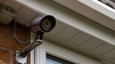 Cámara de vigilancia tipo bala instalada bajo el alero de una vivienda en una pared de ladrillo.
