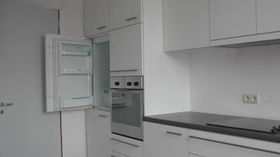 Cocina moderna en tonos blancos y grises con la puerta de la nevera integrada abierta.
