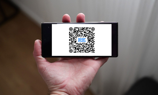 Mano sujetando un teléfono móvil en posición horizontal que muestra un código QR con el logotipo RZ en el centro.