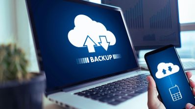 Iconos de una nube con flechas de transferencia y la palabra backup en las pantallas de un ordenador portátil y un teléfono móvil.