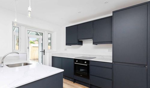 Cocina moderna con mobiliario en color gris oscuro mate y encimera blanca con isla lateral.