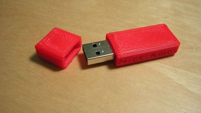 Memoria USB de color rojo con carcasa impresa en 3D sobre una superficie de madera.