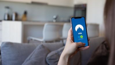 Una persona sosteniendo un teléfono móvil con la aplicación de NordVPN abierta en el salón de una casa.