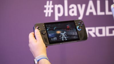 Primer plano de una consola portátil ROG de color negro mostrando un videojuego en pantalla mientras una persona la sujeta con una mano.