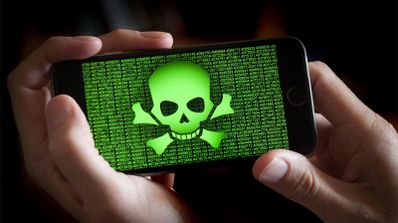 Manos sujetando un teléfono móvil cuya pantalla muestra una calavera verde sobre código binario, representando una infección por malware.