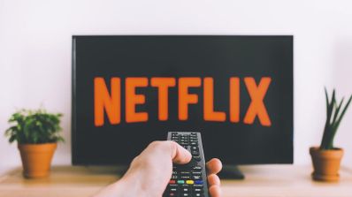 Mano sujetando un mando a distancia frente a un televisor con el logotipo de Netflix en pantalla.