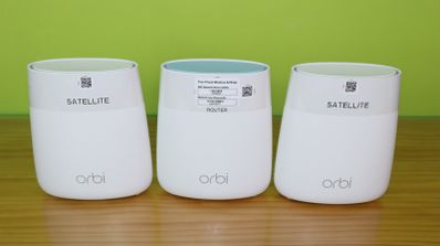 Tres nodos blancos del sistema mesh NETGEAR Orbi colocados en fila sobre una mesa de madera.