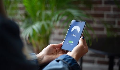 Persona sosteniendo un teléfono móvil con una aplicación de VPN activada en la pantalla.