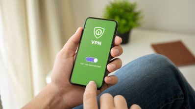 Persona activando una aplicación de VPN en un smartphone con fondo verde e icono de escudo.